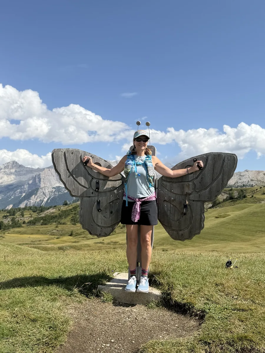Jill playfully holding wooden butterfly wings on a sunny mountain trail