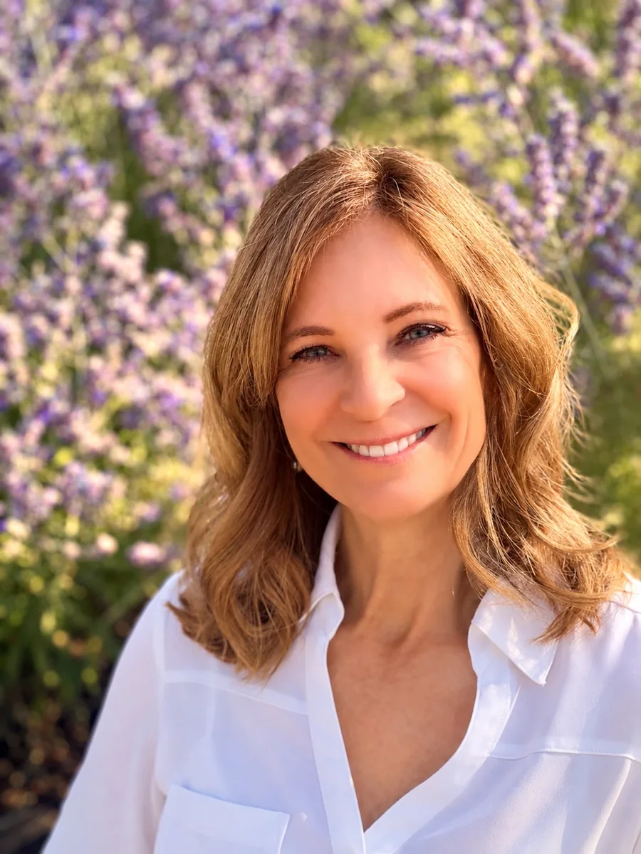 Jill smiling in a white blouse in front of blooming lavender