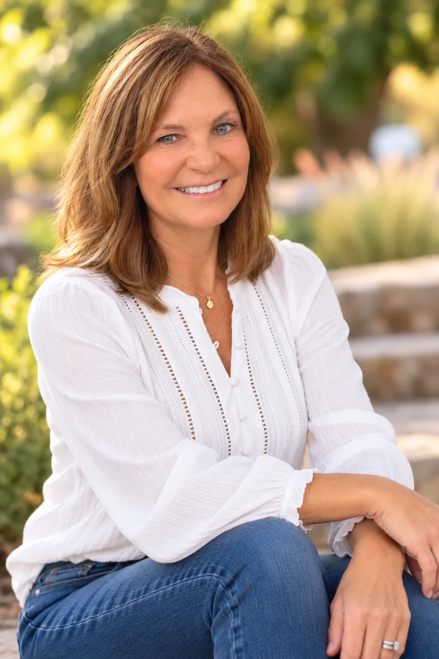 Jill seated outdoors, smiling in a white blouse and blue jeans